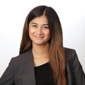 Corporate headshot of a woman with long dark hair in a gray blazer on a white background
