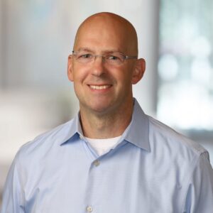 Employee headshot of a man in a light blue shirt with a bright office background