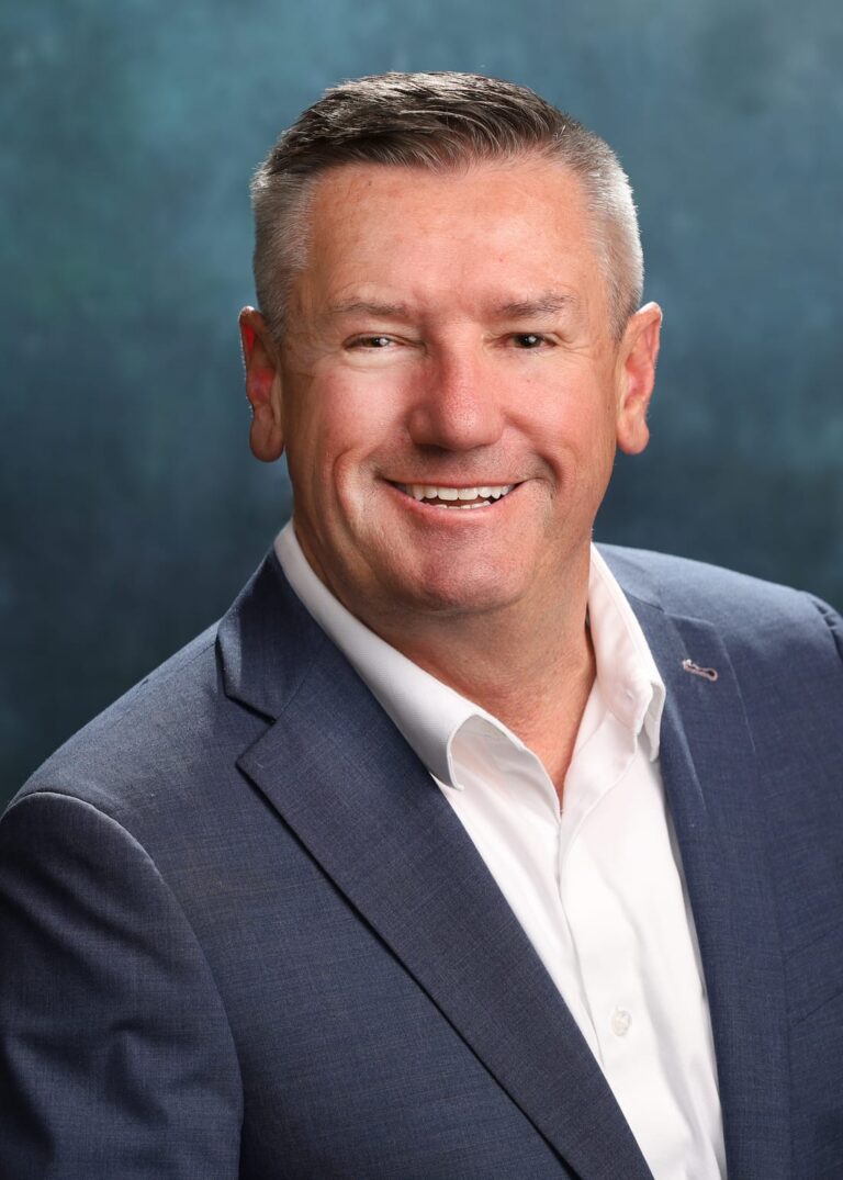 Executive headshot of a man in a blue suit jacket and white shirt on a teal painted backdrop