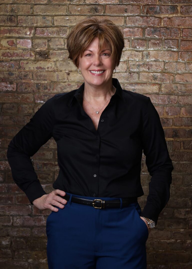 Executive portrait of a woman in a black blouse and navy trousers in front of the brick wall at the Five Star SEO studio in Freehold, NJ