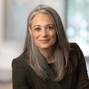 Professional headshot of a woman in a tweed blazer with a soft window background